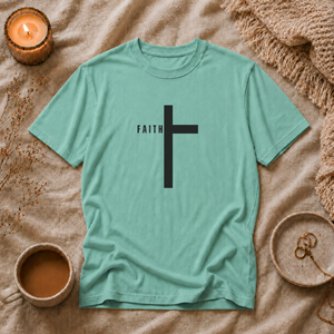 Green t-shirt with a black cross and 'FAITH' text on a textured surface with a candle and cup.