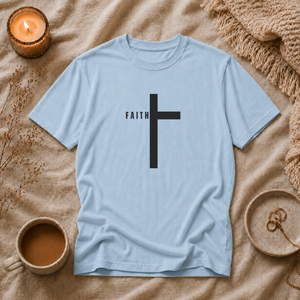 Light blue t-shirt with a black cross and 'FAITH' text on a beige surface with a candle and cup.